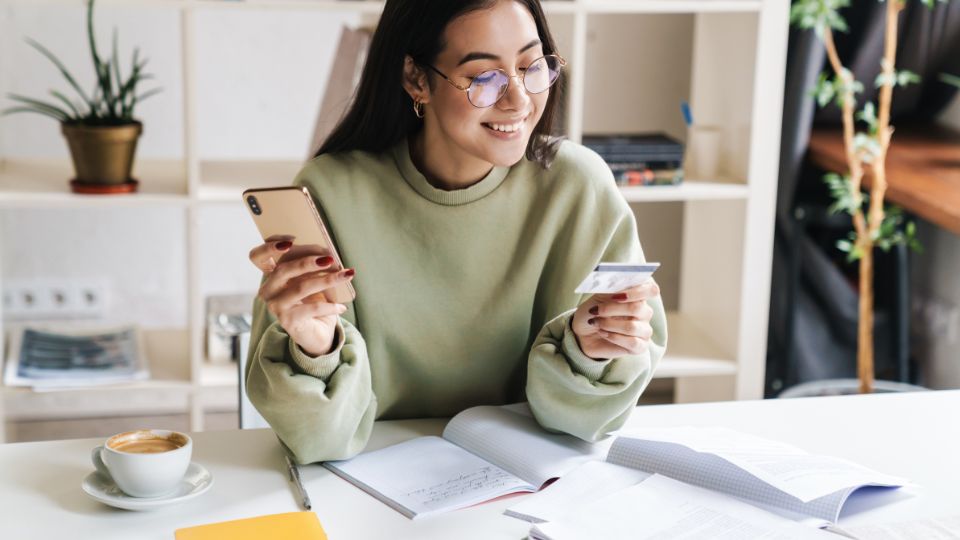smiling young woman with glasses paying rent online with her smartphone and credit card